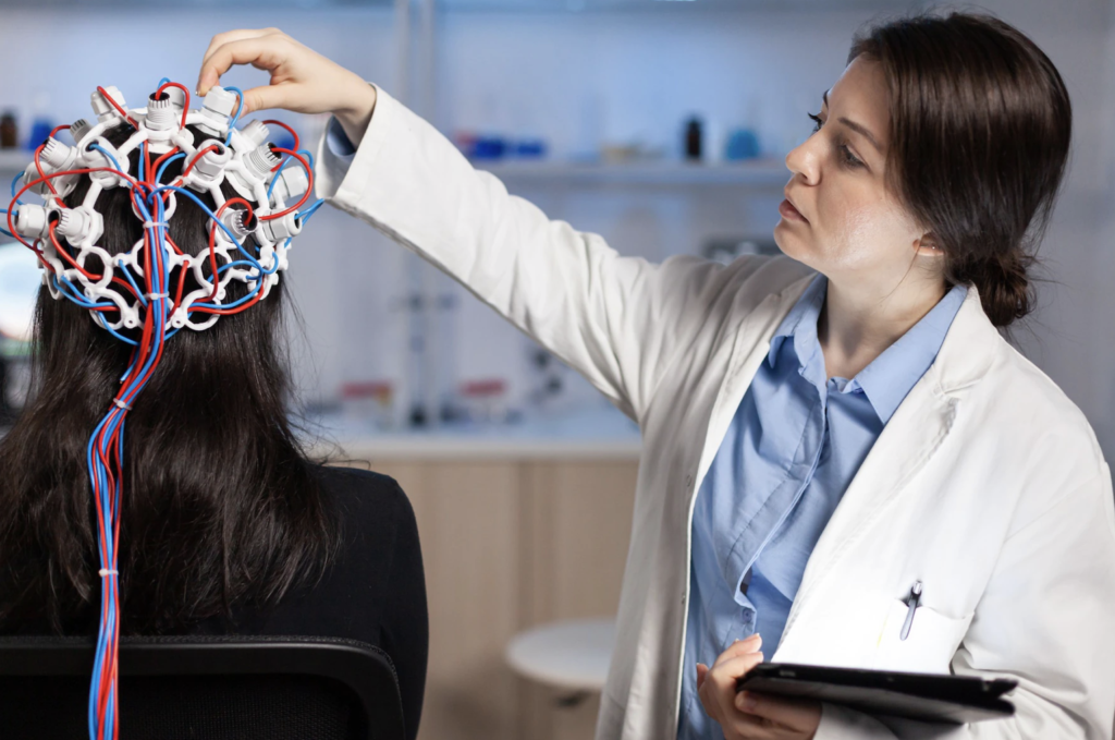 Image showing doctor performing EEG or electroencephalogram on a patient. Doctor has attached multiple metal flat disc electrodes on patient scalp to get data of patient’s sleep cycle which is used to diagnose sleep bruxism.